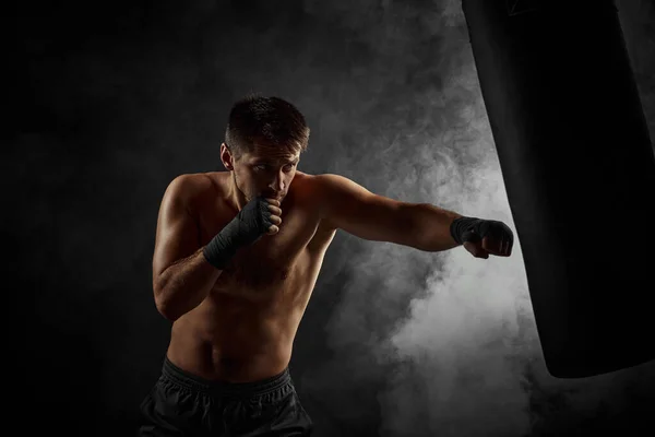 Мужчина боксер бьет в боксерскую сумку на черном фоне — стоковое фото