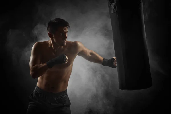 boxer in black boxing wraps punching in boxing bag