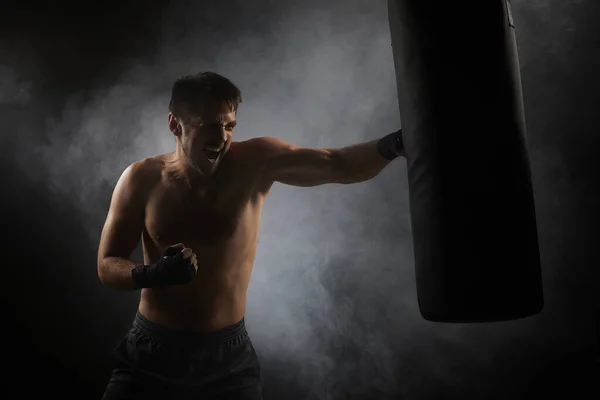 Боксер в чорних боксерських обгортаннях, пробиваючи в боксерському мішку — стокове фото