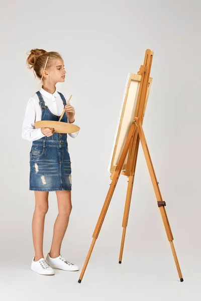 Портрет красивої дівчинки, що тримає дерев'яну художню палітру та пензлик на студійному фоні — стокове фото