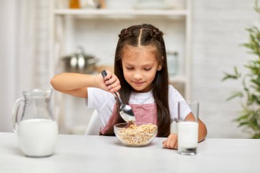 Küçük tatlı kız kahvaltı yapıyor: mısır gevreği ve süt.