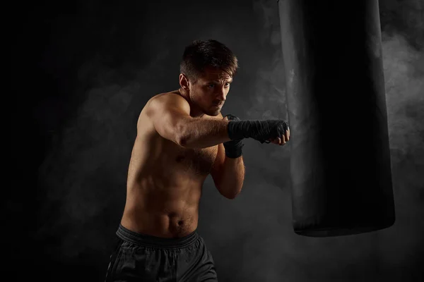 Boxeador masculino perforando en bolsa de boxeo sobre fondo negro —  Fotos de Stock