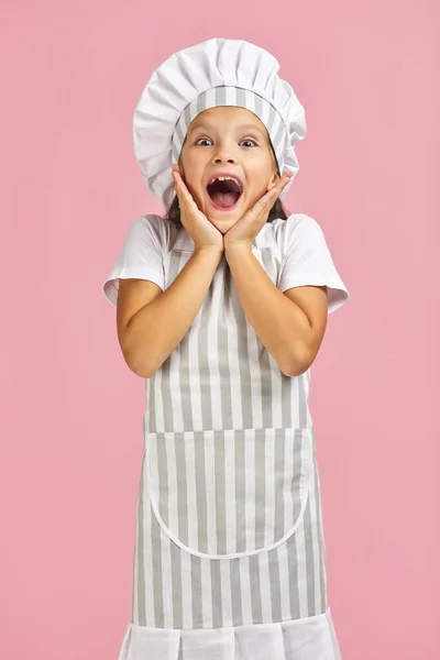 Überraschte kleines Mädchen mit Kochmütze und Schürze — Stockfoto