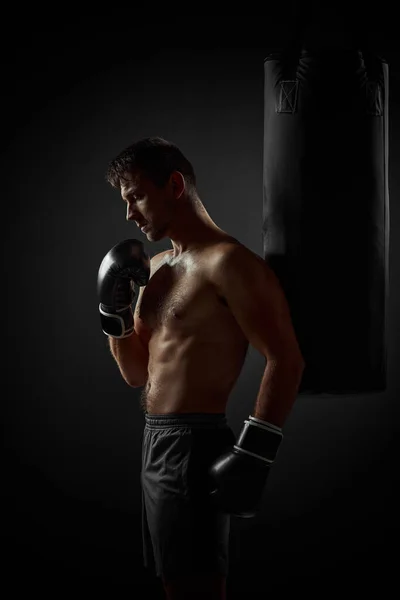 Боксер в черных перчатках стоит рядом с боксерской грушей — стоковое фото
