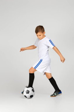 Kıyafetli küçük çocuk futbol topuyla oynuyor.