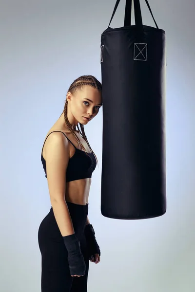 athletic woman in black boxing bandages leaning on punching bag