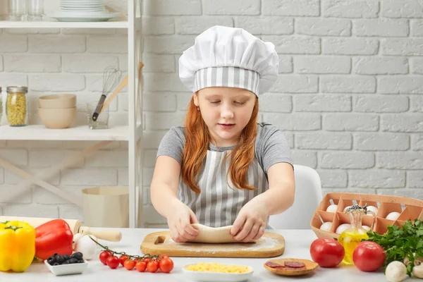 Kleines Mädchen mit Mütze und Schürze kneten den Teig — Stockfoto