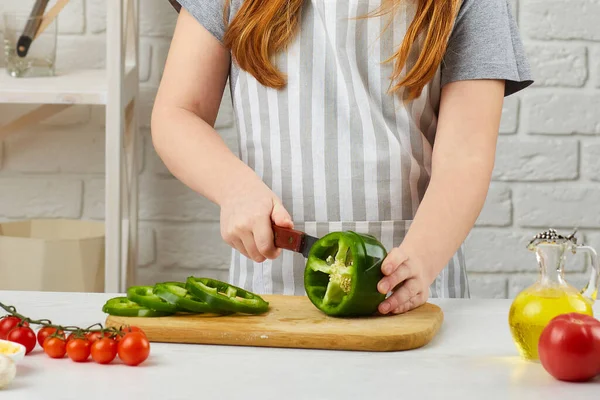 Kleines Mädchen mit Kochmütze und Schürze, die grünen Pfeffer schneidet — Stockfoto