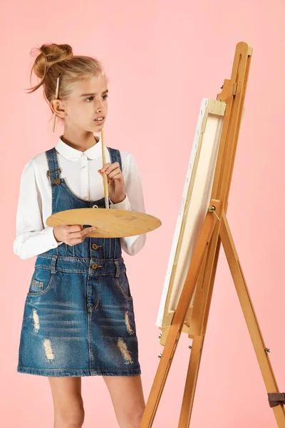 Портрет красивой маленькой девочки с деревянной палитрой и кистью на фоне студии — стоковое фото