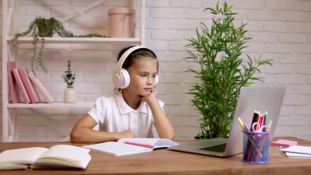 Küçük kız evde okul işleri için dizüstü bilgisayar kullanıyor ve notlar yazıyor.. — Stok video