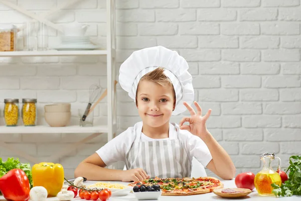 Egy kisfiú séf kalapban és egy kötény főzés pizza — Stock Fotó