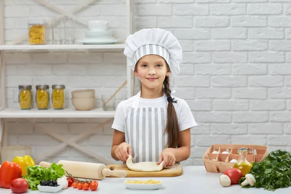 Kleines Mädchen mit Mütze und Schürze kneten den Teig — Stockfoto