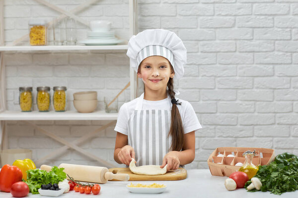 little child girl in cap and an apron knead the dough