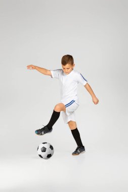 Kıyafetli küçük çocuk futbol topuyla oynuyor.