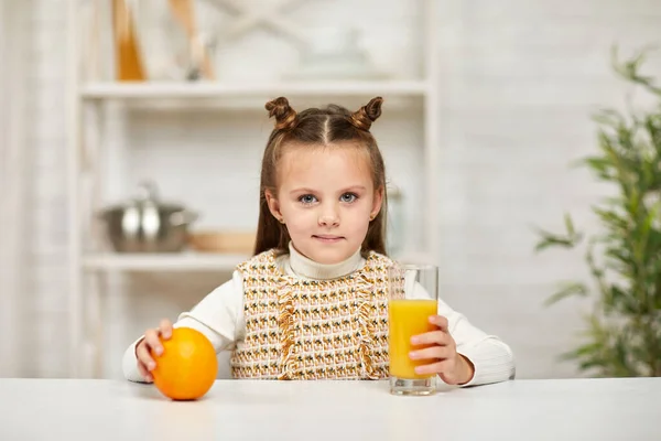 Маленькая девочка с апельсинами и соком на кухне. — стоковое фото