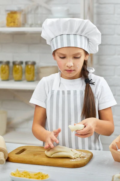 Kleines Mädchen mit Mütze und Schürze kneten den Teig — Stockfoto