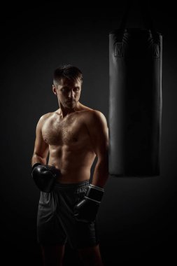 Siyah eldivenli boksör kum torbasının yanında duruyor.