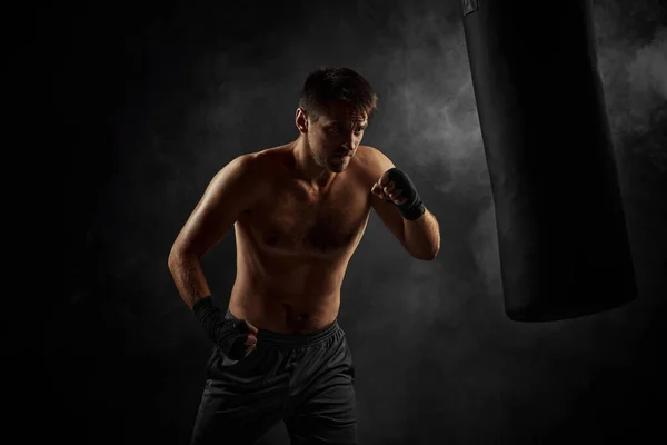 Boxeador masculino perforando en bolsa de boxeo sobre fondo negro — Foto de Stock