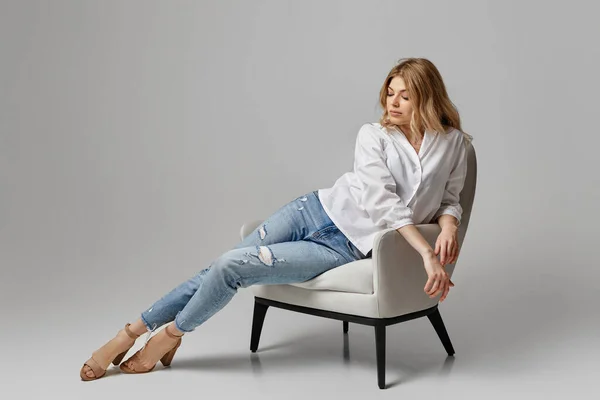 Mulher em jeans e uma camisa branca sentada em poltrona — Fotografia de Stock