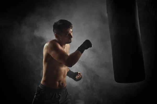 Boxer in schwarzen Boxhüllen boxt in Boxsack — Stockfoto