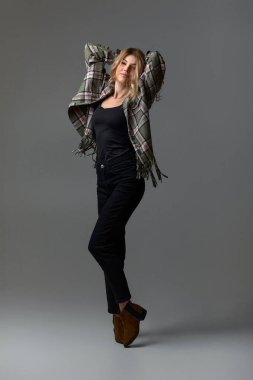 Ceketli, kıvırcık saçlı güzel sarışın kadın stüdyo arka planında sandalyede oturuyor..