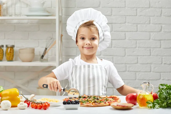 Egy kisfiú séf kalapban és egy kötény főzés pizza — Stock Fotó