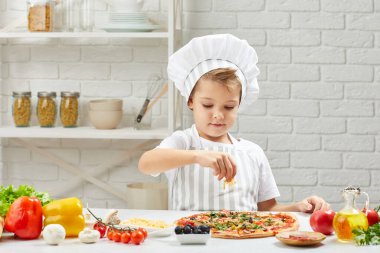 Aşçı şapkalı küçük çocuk ve pizza pişiren önlük.