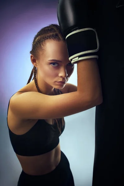 Mujer atlética en guantes de boxeo negro apoyados en el saco de boxeo —  Fotos de Stock