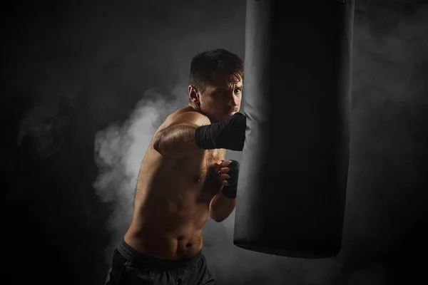Боксер в чорних боксерських обгортаннях, пробиваючи в боксерському мішку — стокове фото