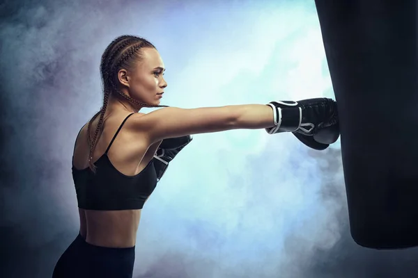 Γυναίκα σε γάντια πυγμαχίας και αθλητικά ρούχα κλοτσιά τσάντα — Φωτογραφία Αρχείου