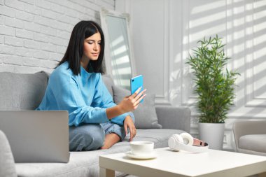 Evde akıllı telefon kullanan bir kadın..