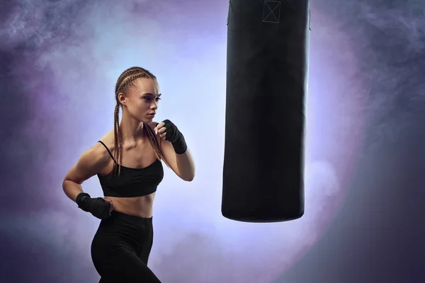 Mulher com bandagens de boxe batendo o saco de boxe — Fotografia de Stock