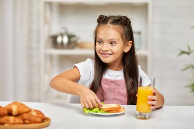 Küçük kız kahvaltı yapıyor. Sandviç ve portakal suyu.