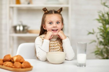 Küçük kız kahvaltı yapıyor: mısır gevreği ve mutfakta süt..