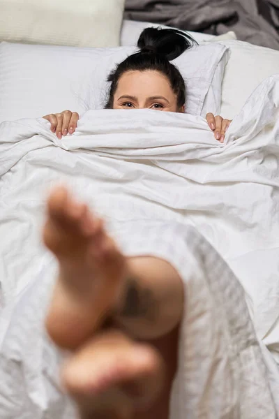 Mulher está deitada na cama e se escondendo sob cobertor — Fotografia de Stock