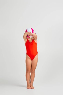 Mayo giymiş, gözlüklü ve yüzme şapkalı küçük bir kız çocuğu. Tam uzunluk