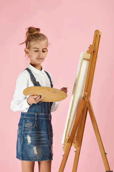 Portrait of beautiful little girl holding a wooden art palette and brush on studio background — Stock Photo, Image