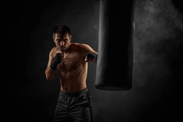 Man bokser ponsen in bokszak op zwarte achtergrond — Stockfoto