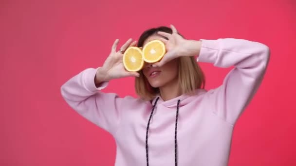 Femme en vêtements roses décontractés tenant des oranges et dansant — Video