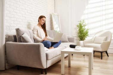 Evde dizüstü bilgisayar kullanan genç bir kadın.