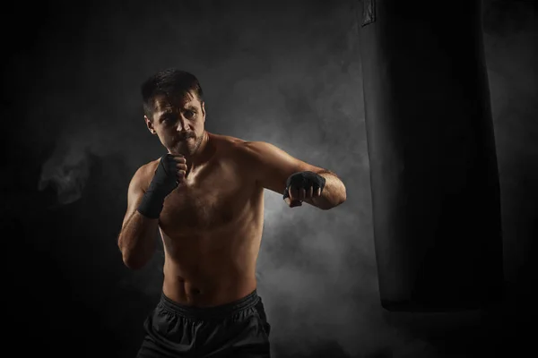Boxeador en boxeo negro envuelve perforación en bolsa de boxeo — Foto de Stock