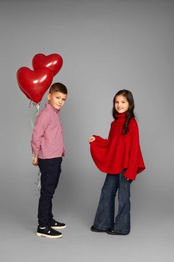 Kırmızı kalp balonları olan bir çift küçük kız ve oğlan.