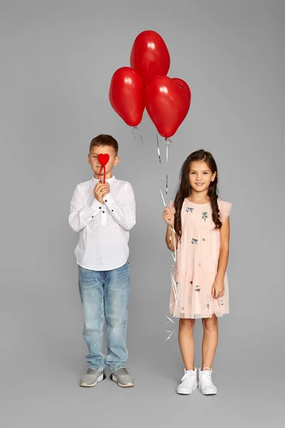 Pareja de niña y niño con globos de corazón rojo — Foto de Stock