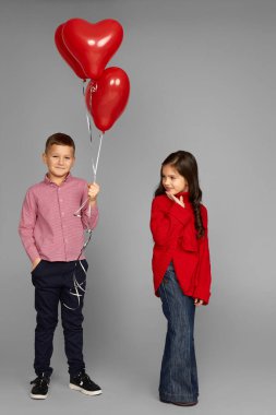 Kırmızı kalp balonları olan bir çift küçük kız ve oğlan.