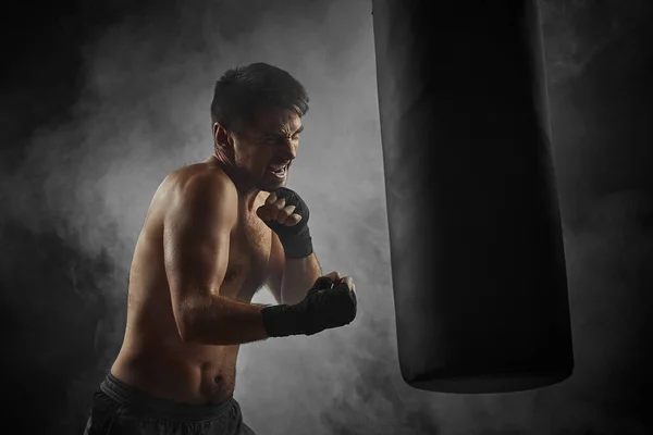 boxer in black boxing wraps punching in boxing bag