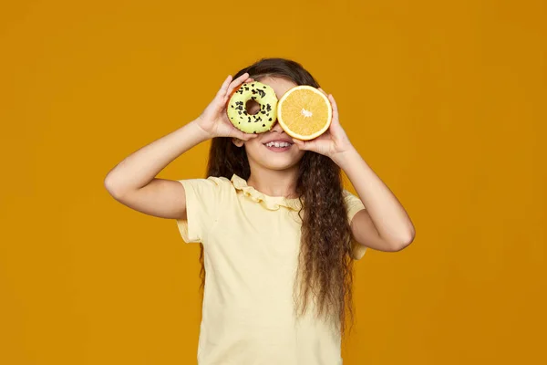 Дитяча дівчина тримає шоколадний пончик і свіжий апельсин — стокове фото