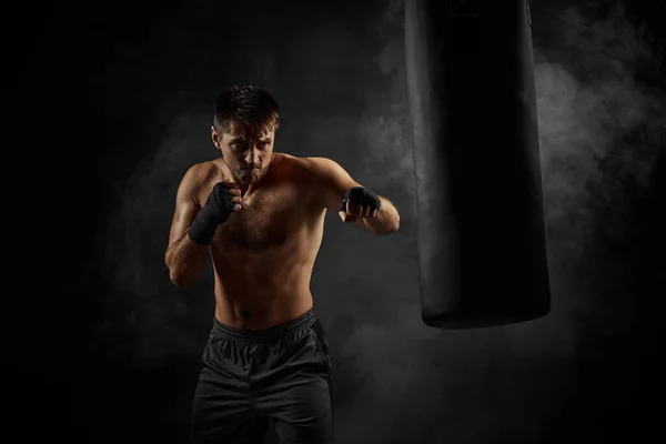 Boxeador masculino perforando en bolsa de boxeo sobre fondo negro — Foto de Stock