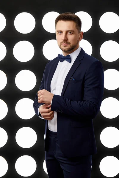 Hombre guapo en esmoquin posando contra el telón de fondo de focos — Foto de Stock