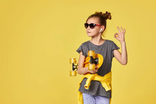 Menina em óculos de sol posando com skate amarelo — Fotografia de Stock