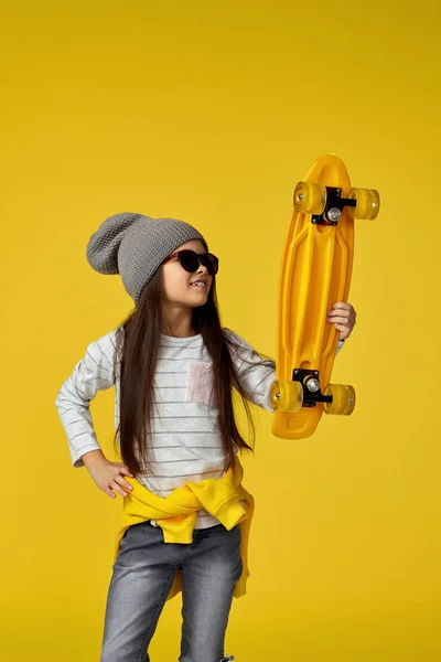 Enfant fille en chapeau et lunettes de soleil avec skateboard jaune — Photo